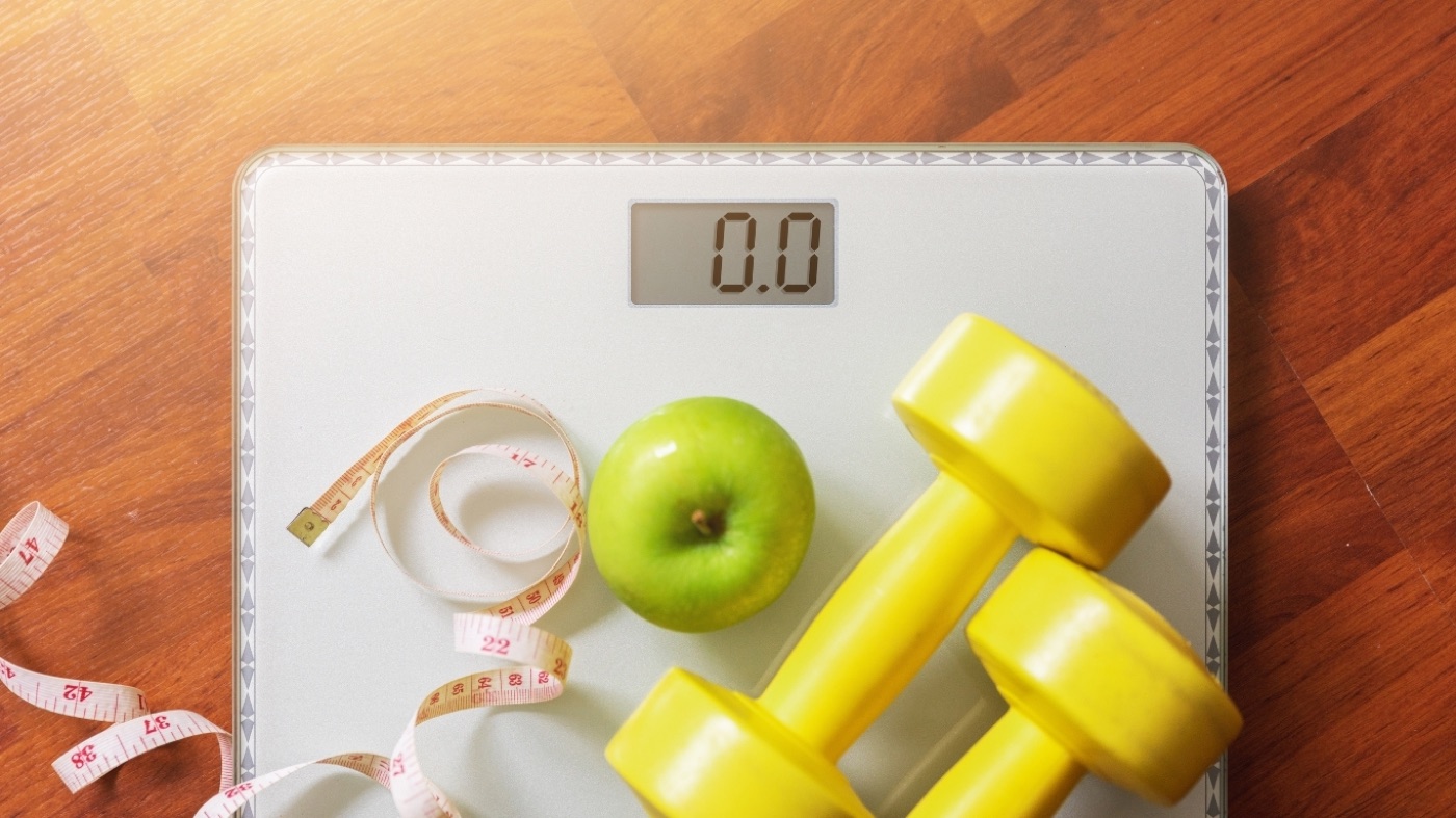 Scale with dumbbells and apple representing a holistic approach to metabolic health